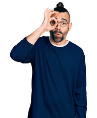 Hispanic man with ponytail wearing casual sweater and glasses doing ok gesture shocked with surprised face, eye looking through fingers. unbelieving expression.