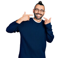 Hispanic man with ponytail wearing casual sweater and glasses smiling cheerful showing and pointing...