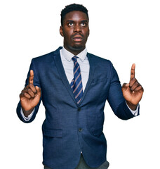 Handsome business black man wearing business suit and tie amazed and surprised looking up and pointing with fingers and raised arms.