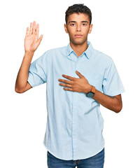 Young handsome african american man wearing casual clothes swearing with hand on chest and open...