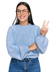 Young hispanic woman wearing casual clothes and glasses smiling with happy face winking at the...
