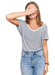 Beautiful young blonde woman wearing casual clothes and glasses smiling and laughing with hand on face covering eyes for surprise. blind concept.