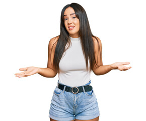 Young beautiful hispanic girl wearing casual clothes clueless and confused expression with arms and...