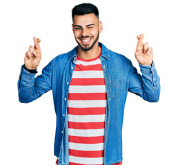 Young hispanic man with beard doing fingers crossed luck gesture winking looking at the camera with...