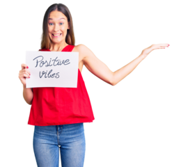 Beautiful brunette young woman holding positive vibes banner celebrating victory with happy smile and winner expression with raised hands