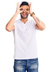 Fototapeta premium Young handsome hispanic man wearing casual clothes doing ok gesture like binoculars sticking tongue out, eyes looking through fingers. crazy expression.