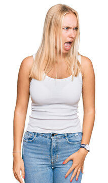 Young blonde girl wearing casual style with sleeveless shirt angry and mad screaming frustrated and furious, shouting with anger. rage and aggressive concept.