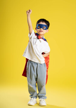full body image of a boy wearing a superhero shirt posing on a yellow background