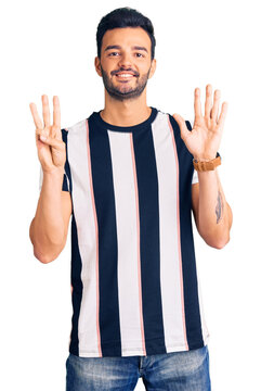 Young handsome hispanic man wearing striped tshirt showing and pointing up with fingers number eight while smiling confident and happy.