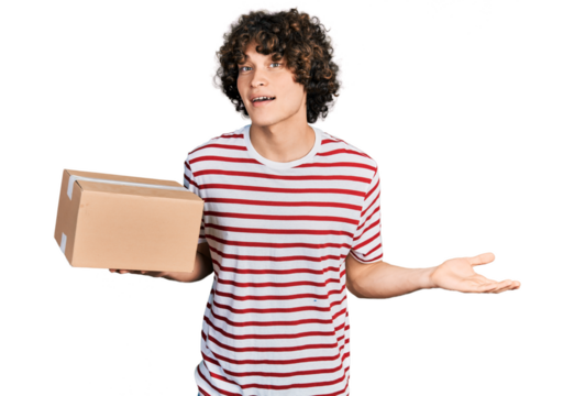 Caucasian teenager holding delivery package celebrating achievement with happy smile and winner expression with raised hand