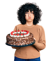 Young hispanic couple celebrating birthday with cake puffing cheeks with funny face. mouth inflated...
