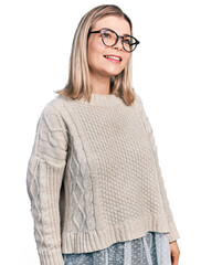 Young blonde woman wearing glasses looking away to side with smile on face, natural expression. laughing confident.