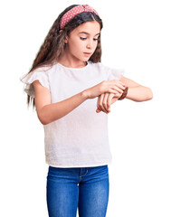 Cute hispanic child girl wearing casual white tshirt checking the time on wrist watch, relaxed and confident