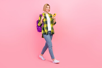 Full length photo of attractive young woman walk reading news gadget wear trendy plaid yellow clothes isolated on pink color background