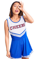 Fototapeta premium Young beautiful chinese girl wearing cheerleader uniform doing ok gesture with hand smiling, eye looking through fingers with happy face.