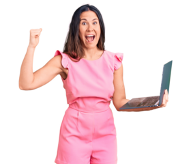 Young beautiful brunette woman working using laptop screaming proud, celebrating victory and success very excited with raised arms
