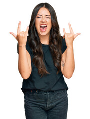 Beautiful brunette young woman wearing black shirt shouting with crazy expression doing rock symbol with hands up. music star. heavy concept.