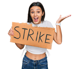 Young hispanic girl holding strike banner cardboard celebrating victory with happy smile and winner expression with raised hands
