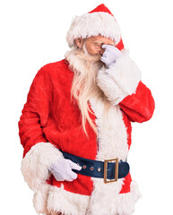 Old senior man with grey hair and long beard wearing traditional santa claus costume tired rubbing nose and eyes feeling fatigue and headache. stress and frustration concept.