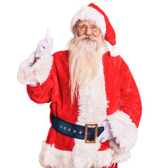 Old senior man with grey hair and long beard wearing traditional santa claus costume showing and pointing up with finger number one while smiling confident and happy.