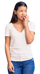 Fototapeta premium Young beautiful latin girl wearing casual white t shirt looking stressed and nervous with hands on mouth biting nails. anxiety problem.