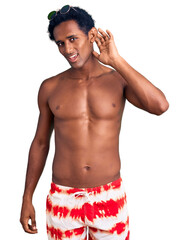 Fototapeta premium African handsome man wearing swimsuit and sunglasses smiling with hand over ear listening an hearing to rumor or gossip. deafness concept.