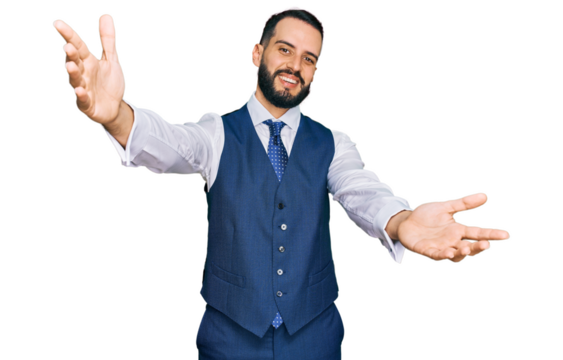 Young man with beard wearing business vest looking at the camera smiling with open arms for hug. cheerful expression embracing happiness.