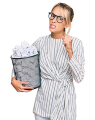 Beautiful blonde business woman holding paper bin full of crumpled papers annoyed and frustrated shouting with anger, yelling crazy with anger and hand raised