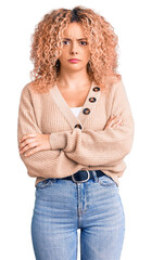 Young blonde woman with curly hair wearing casual winter jumper skeptic and nervous, disapproving expression on face with crossed arms. negative person.