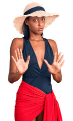 Young african american woman wearing swimsuit and summer hat moving away hands palms showing refusal and denial with afraid and disgusting expression. stop and forbidden.