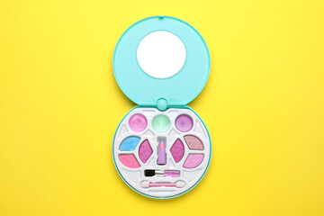 Decorative cosmetics for kids. Eye shadow palette with lipstick on yellow background, top view