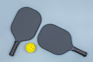 Closeup top view of two black pickleball paddles and a yellow ball on light gray background with copy space