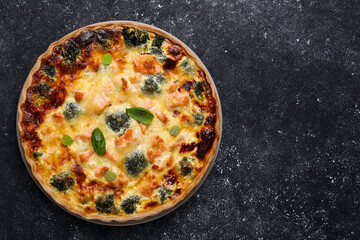 Delicious homemade quiche with salmon and broccoli on black table, top view. Space for text