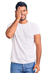 Young latin man wearing casual clothes covering one eye with hand, confident smile on face and surprise emotion.