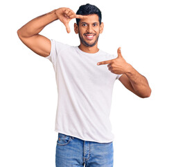 Fototapeta premium Young latin man wearing casual clothes smiling making frame with hands and fingers with happy face. creativity and photography concept.