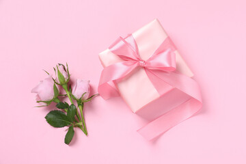 Gift box and beautiful rose flowers on pink background, flat lay