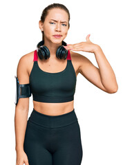 Beautiful blonde woman wearing gym clothes and using headphones cutting throat with hand as knife, threaten aggression with furious violence