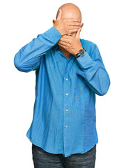 Middle age bald man wearing casual clothes covering eyes and mouth with hands, surprised and shocked. hiding emotion