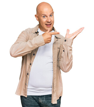 Middle age bald man wearing casual clothes amazed and smiling to the camera while presenting with hand and pointing with finger.