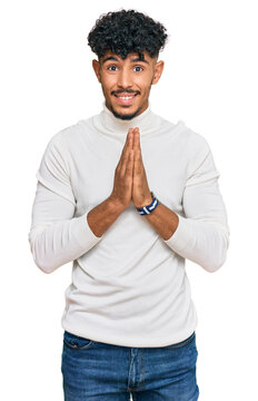 Young arab man wearing casual winter sweater praying with hands together asking for forgiveness smiling confident.