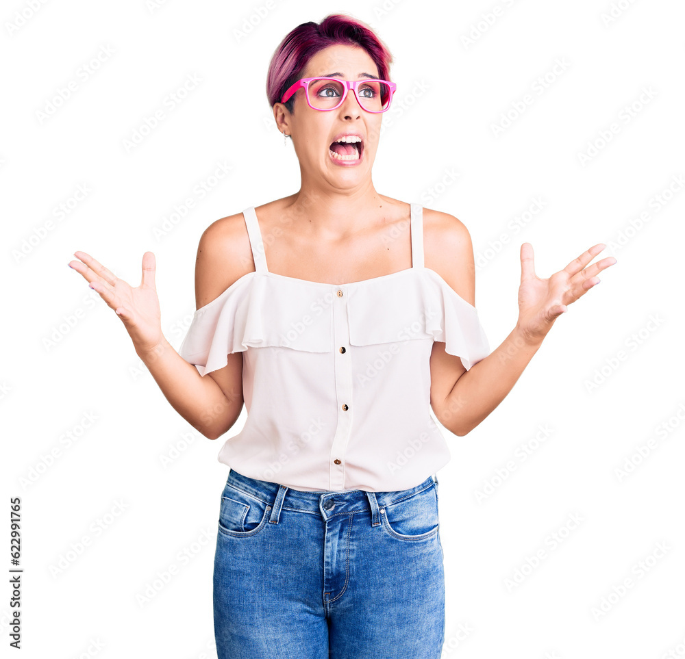 Canvas Prints Young beautiful woman with pink hair wearing casual clothes and glasses crazy and mad shouting and yelling with aggressive expression and arms raised. frustration concept.