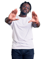 Fototapeta premium Young african american man with braids wearing casual white tshirt doing frame using hands palms and fingers, camera perspective