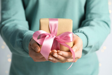 Woman holding gift box with pink bow on light grey background, closeup