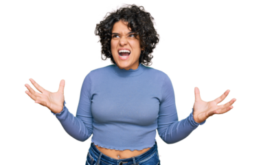 Young hispanic woman with curly hair wearing casual clothes crazy and mad shouting and yelling with aggressive expression and arms raised. frustration concept.