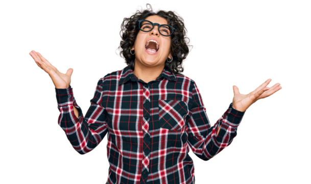 Young hispanic woman with curly hair wearing casual clothes and glasses crazy and mad shouting and yelling with aggressive expression and arms raised. frustration concept.