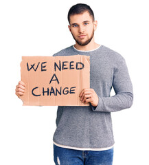 Young handsome man holding we need a change banner thinking attitude and sober expression looking self confident