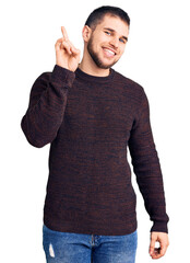 Young handsome man wearing casual sweater showing and pointing up with finger number one while smiling confident and happy.