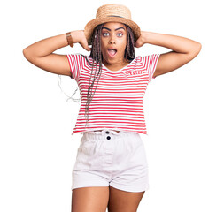 Young african american woman with braids wearing summer hat crazy and scared with hands on head, afraid and surprised of shock with open mouth