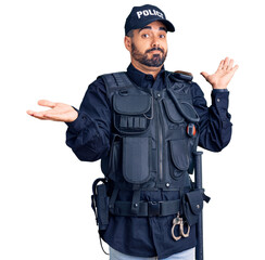 Young hispanic man wearing police uniform clueless and confused expression with arms and hands...