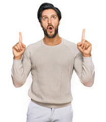 Young hispanic man wearing casual clothes amazed and surprised looking up and pointing with fingers and raised arms.